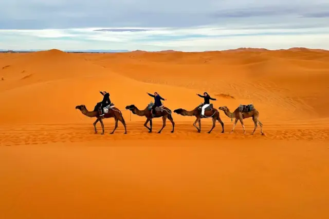 Viajeros a lomo de dromedario atravesando al atardecer las dunas de Erg Chebbi, en Merzouga