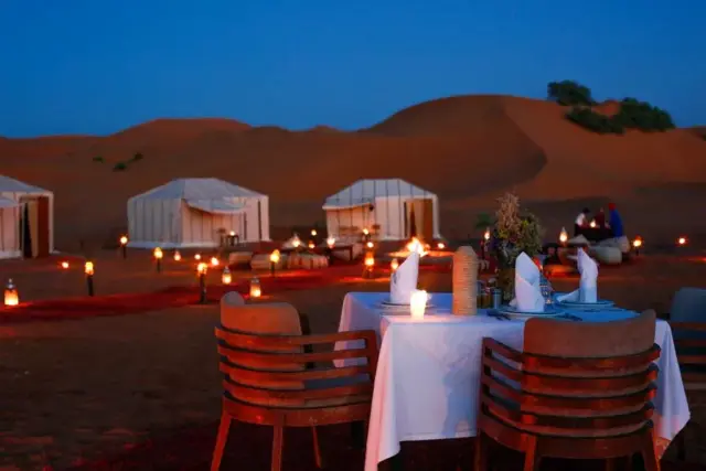 Mesa para dos con farolitos encendidos entre las dunas de Merzouga al anochecer